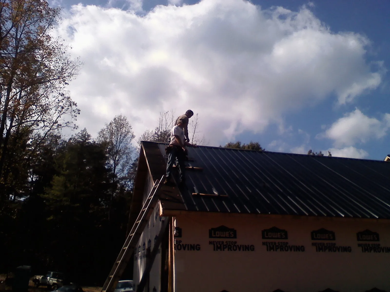 Roofer fastening dark metal panels high against a cloudy sky, from a Roof Inspection job in Oceanport