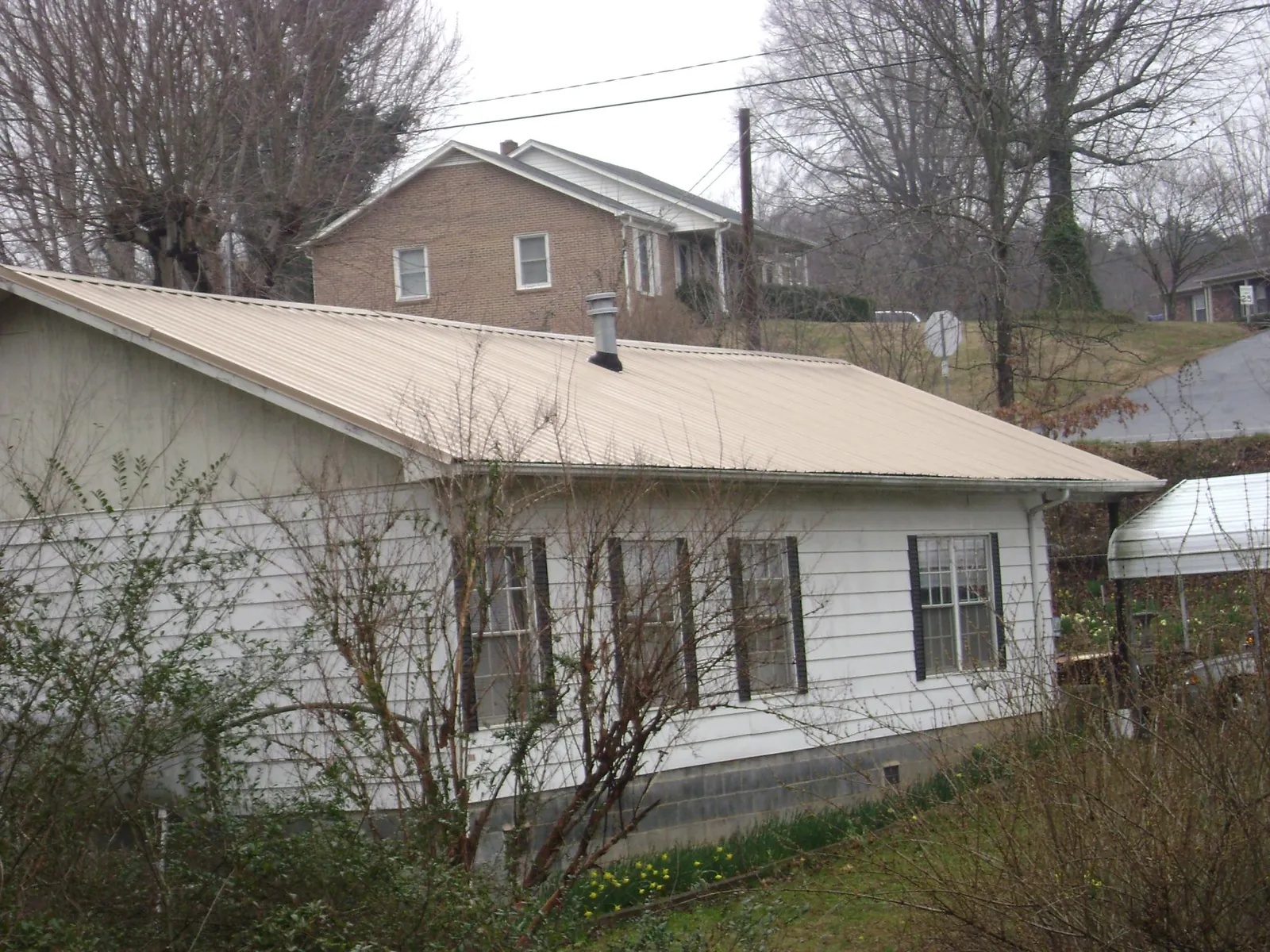 Tan metal roof on a white sided house set into a hillside — Commercial Roofing by Roofing Brothers in Oceanport